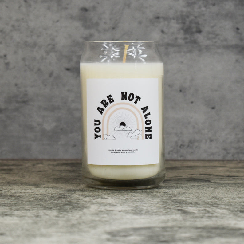 
            
                Load image into Gallery viewer, Vanilla &amp;amp; Cedar scent soy wax candle in can shaped glass vessel with tapered top and artistic hand-lettered label saying &amp;quot;You are not alone&amp;quot;
            
        